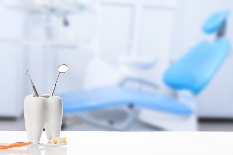 Stock image of a healthy white tooth and dentist mirror with explorer probe instrument near toothbrush against blurred dentist Office background with dental chair and lamp.
