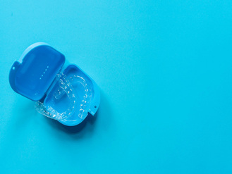 Clear dental aligner placed inside open blue plastic case on bright blue background.